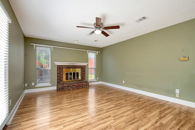 unfurnished living room featuring a brick fireplace, a textured ceiling, light hardwood / wood-style flooring, and ceiling fan