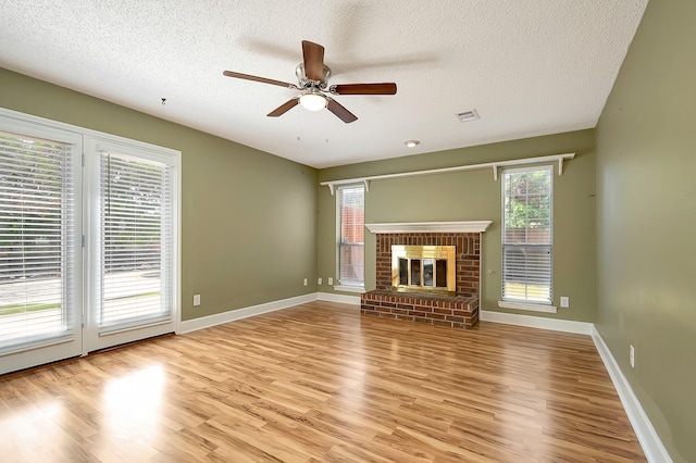 unfurnished living room featuring ceiling fan, a textured ceiling, light wood-type flooring, and a fireplace