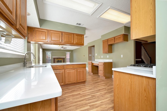 kitchen with kitchen peninsula, ceiling fan, light wood-type flooring, a fireplace, and sink