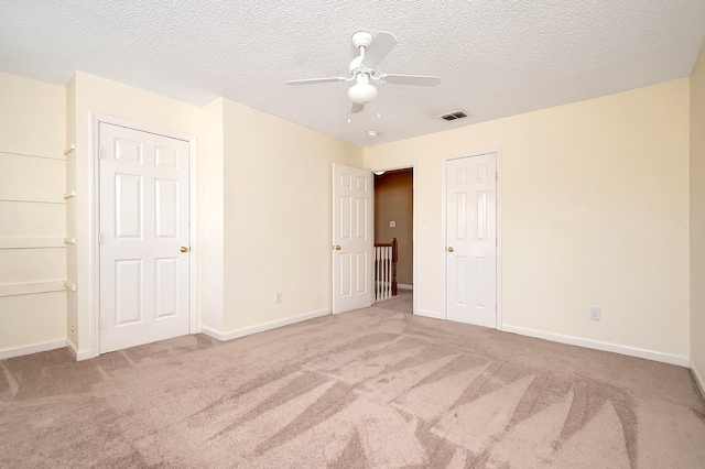 unfurnished bedroom with ceiling fan, light carpet, and a textured ceiling