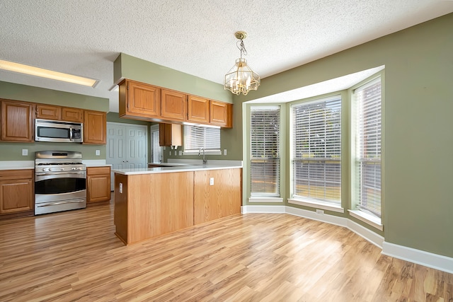 kitchen featuring light wood-type flooring, pendant lighting, kitchen peninsula, a notable chandelier, and appliances with stainless steel finishes