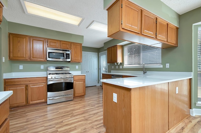 kitchen featuring kitchen peninsula, stainless steel appliances, light wood-type flooring, a textured ceiling, and sink