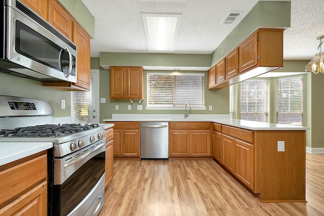 kitchen featuring decorative light fixtures, stainless steel appliances, an inviting chandelier, sink, and light hardwood / wood-style flooring