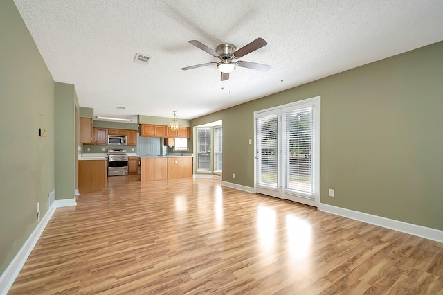 unfurnished living room with light wood-type flooring, ceiling fan with notable chandelier, and a textured ceiling