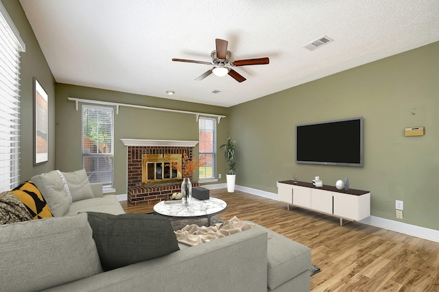 living room with a fireplace, ceiling fan, a wealth of natural light, and light hardwood / wood-style floors