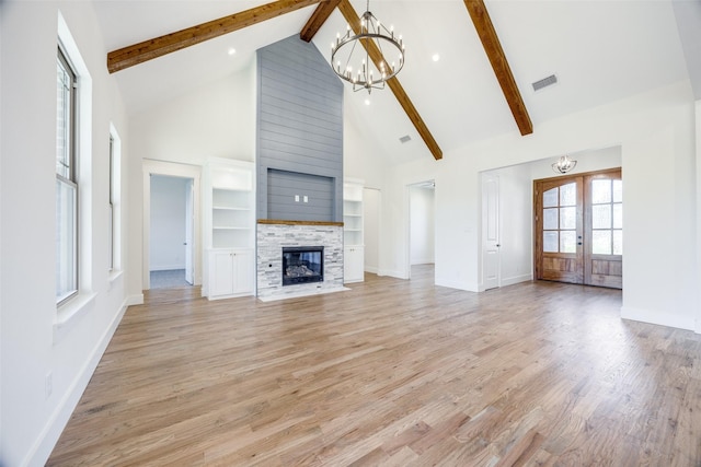 unfurnished living room featuring a fireplace, french doors, high vaulted ceiling, and a chandelier