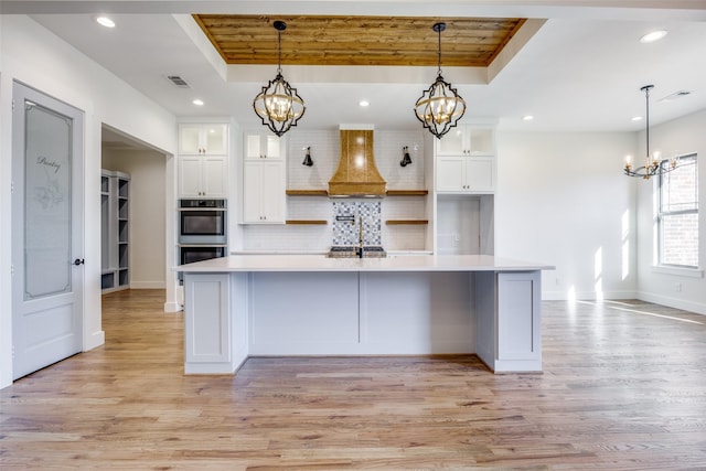 kitchen with hanging light fixtures, double oven, light hardwood / wood-style floors, a tray ceiling, and white cabinets