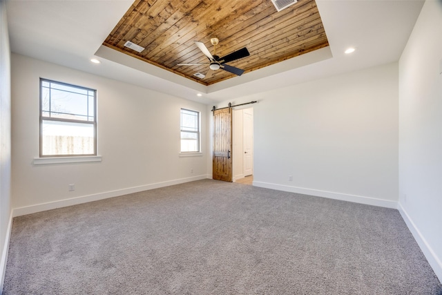 empty room with a tray ceiling, a barn door, carpet, and wooden ceiling