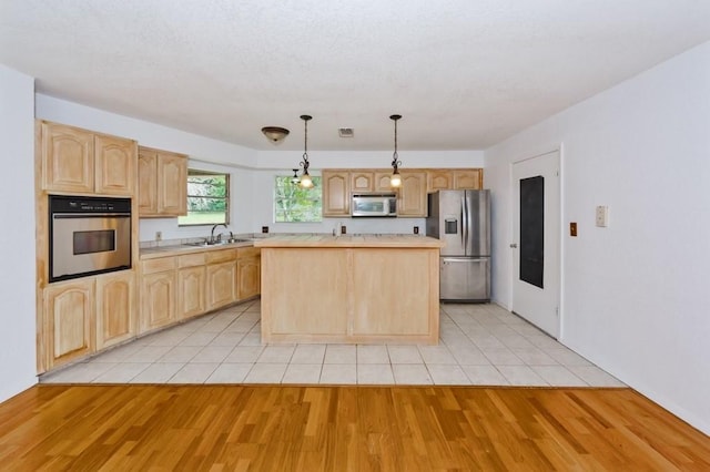 kitchen featuring light brown cabinets, a kitchen island, light countertops, appliances with stainless steel finishes, and a sink