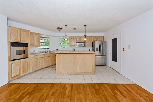 kitchen featuring pendant lighting, appliances with stainless steel finishes, a center island, light brown cabinetry, and light hardwood / wood-style floors