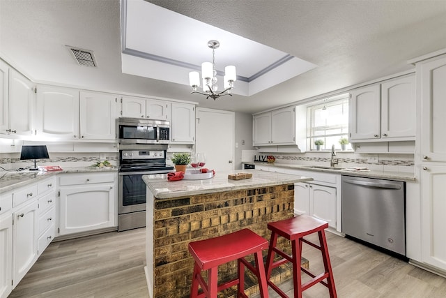 kitchen with an inviting chandelier, white cabinetry, stainless steel appliances, and a tray ceiling