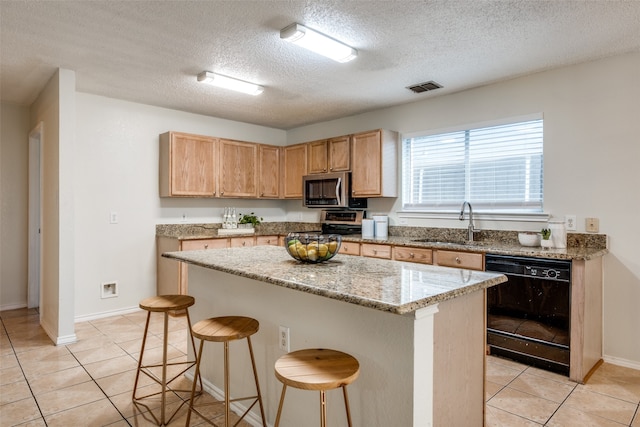 kitchen with appliances with stainless steel finishes, a textured ceiling, sink, a kitchen island, and a breakfast bar area