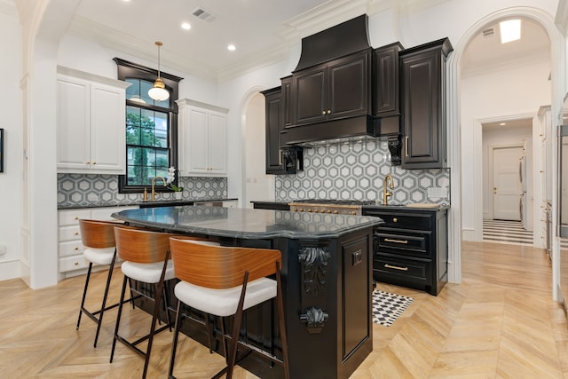 kitchen with decorative backsplash, ornamental molding, a center island, light parquet floors, and white cabinetry