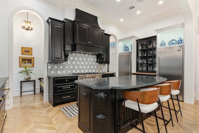 kitchen with a kitchen island, dark stone counters, stainless steel built in fridge, decorative backsplash, and a breakfast bar