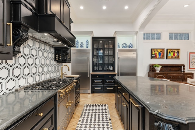 kitchen featuring dark stone countertops, high end appliances, crown molding, light parquet floors, and tasteful backsplash