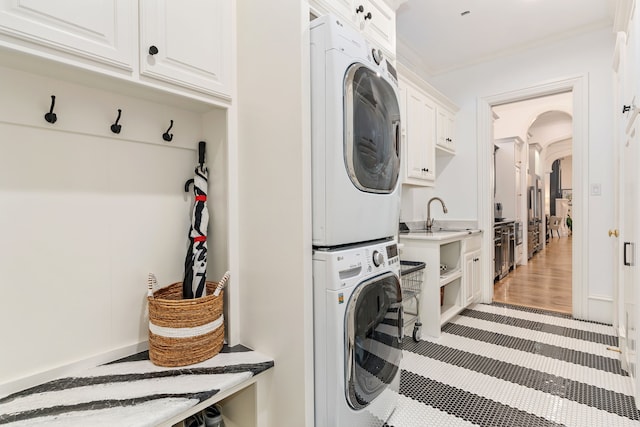 laundry area with sink, light hardwood / wood-style floors, stacked washer and dryer, ornamental molding, and cabinets