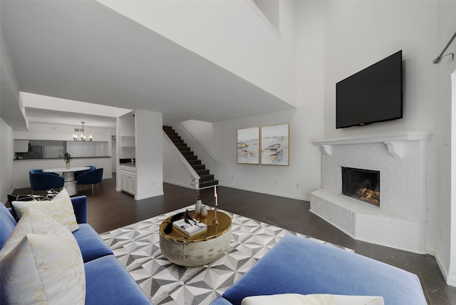 living room featuring a chandelier, a towering ceiling, dark hardwood / wood-style flooring, and a brick fireplace