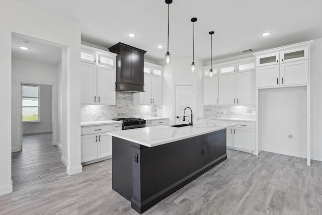 kitchen with stainless steel range with gas stovetop, a kitchen island with sink, sink, and white cabinetry