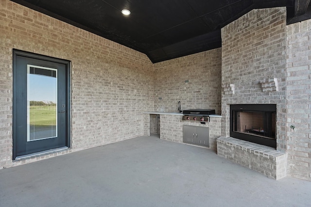 view of patio with exterior kitchen, an outdoor brick fireplace, and grilling area