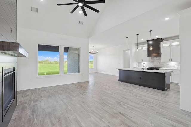 kitchen featuring light wood-type flooring, high vaulted ceiling, a kitchen island with sink, white cabinets, and pendant lighting