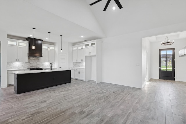 kitchen with premium range hood, an island with sink, decorative light fixtures, light hardwood / wood-style floors, and decorative backsplash