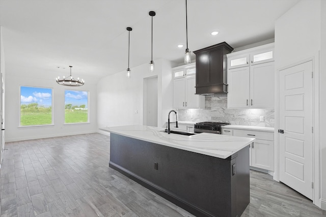 kitchen featuring gas range, white cabinets, sink, and a kitchen island with sink