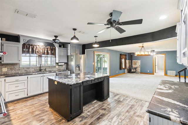 kitchen featuring stainless steel fridge, decorative light fixtures, sink, a wood stove, and a center island