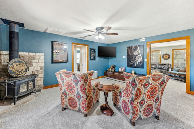 carpeted living room with a wood stove and ceiling fan