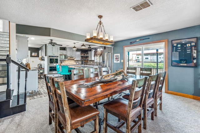 carpeted dining room with ceiling fan with notable chandelier and a textured ceiling