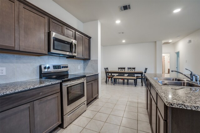 kitchen with light stone countertops, decorative backsplash, sink, light tile patterned flooring, and appliances with stainless steel finishes