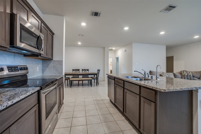 kitchen with an island with sink, light tile patterned floors, sink, backsplash, and appliances with stainless steel finishes