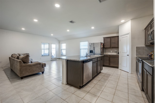 kitchen featuring an island with sink, light stone countertops, stainless steel appliances, tasteful backsplash, and dark brown cabinets