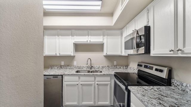 kitchen with appliances with stainless steel finishes, light stone counters, white cabinetry, and sink