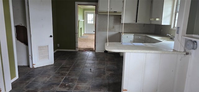 kitchen with kitchen peninsula, white cabinets, sink, and tasteful backsplash