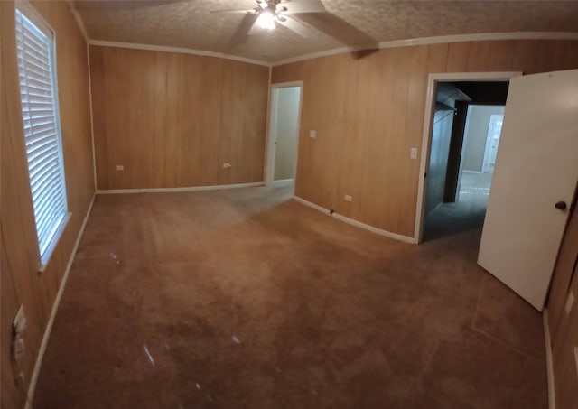 carpeted spare room featuring a textured ceiling, crown molding, wooden walls, and ceiling fan