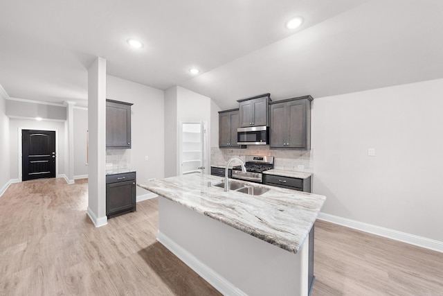 kitchen featuring sink, tasteful backsplash, light wood-type flooring, stainless steel appliances, and a kitchen island with sink