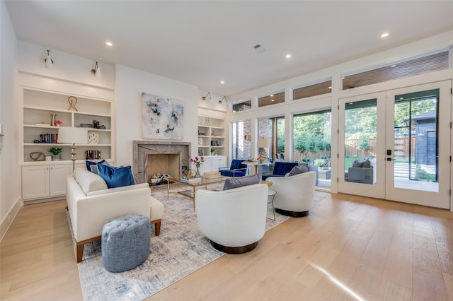 living room featuring french doors, a fireplace, built in features, and light hardwood / wood-style floors