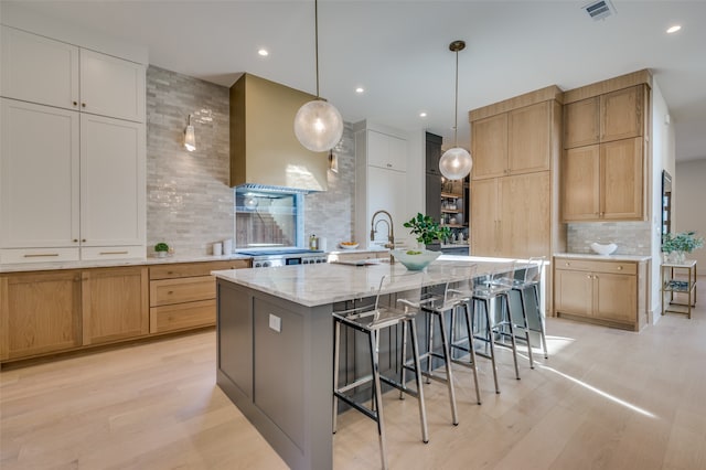 kitchen with tasteful backsplash, decorative light fixtures, range hood, a spacious island, and light stone countertops