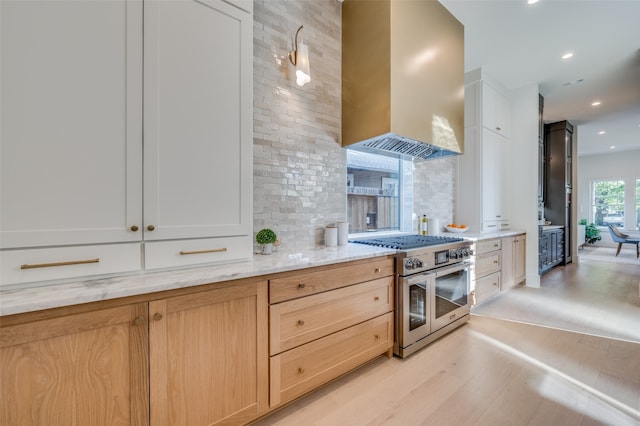 kitchen with wall chimney exhaust hood, double oven range, light hardwood / wood-style floors, and white cabinets