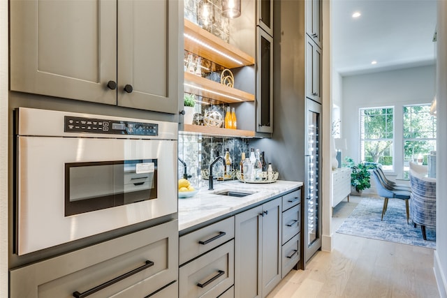 bar featuring light wood-type flooring, sink, tasteful backsplash, gray cabinets, and light stone countertops