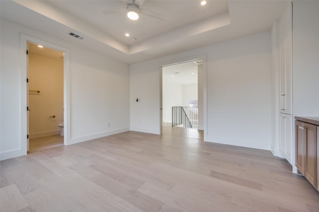 unfurnished room featuring a raised ceiling, light wood-type flooring, and ceiling fan