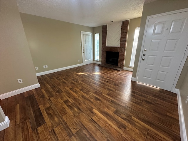 unfurnished living room featuring dark wood-type flooring, a brick fireplace, and a textured ceiling