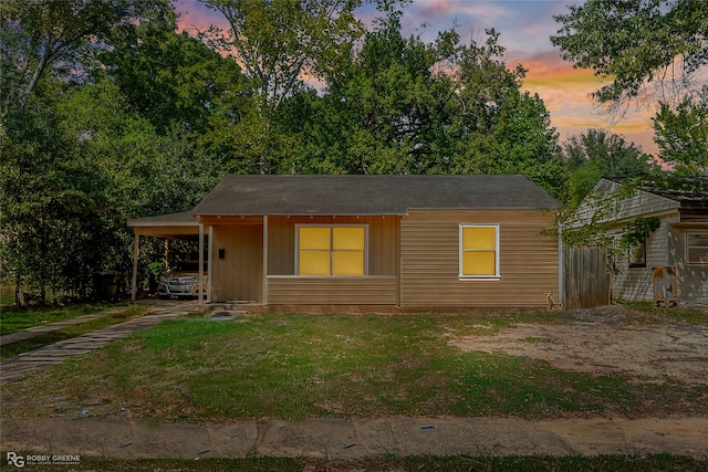 back house at dusk featuring a yard and a carport