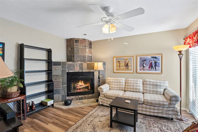 living room with ceiling fan, a tile fireplace, wood-type flooring, and a textured ceiling