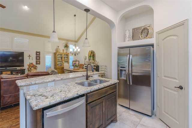 kitchen with stainless steel appliances, dark brown cabinetry, sink, hanging light fixtures, and a kitchen island with sink