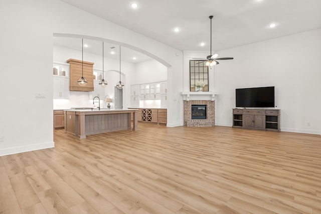 unfurnished living room with a brick fireplace, sink, light hardwood / wood-style flooring, and ceiling fan