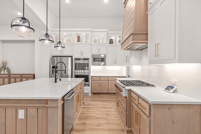 kitchen with pendant lighting, a large island with sink, white cabinets, appliances with stainless steel finishes, and premium range hood