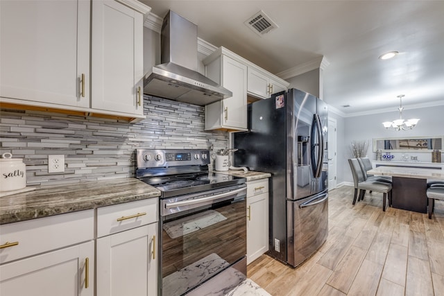 kitchen featuring appliances with stainless steel finishes, wall chimney exhaust hood, white cabinetry, and a chandelier