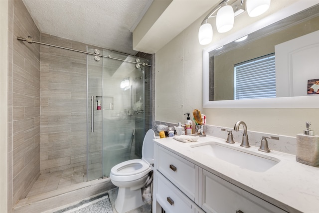 bathroom with a textured ceiling, a shower with door, vanity, and toilet