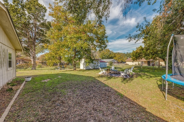 view of yard featuring a storage shed, a trampoline, fence, and an outbuilding